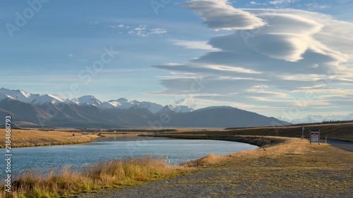 Winding river valley at sunset with golden grasses, snowy mountains on horizon, expansive blue sky and wispy clouds, tranquil outdoor landscape motion scene