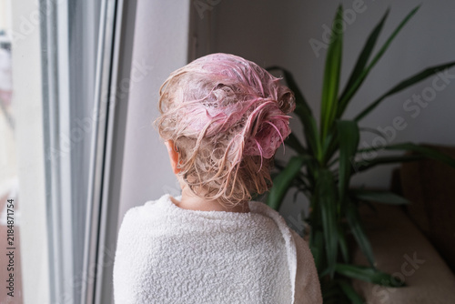 Фотография Rear view of little girl with pink temporary hair dye wrapped in towel at home