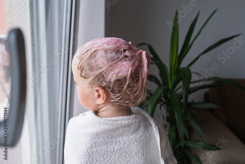 Фотография Rear view of little girl with pink temporary hair dye wrapped in towel at home