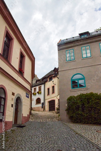 Fotografía Eine enge Kopfsteinpflastergasse führt zwischen unterschiedlich gestalteten historischen Häusern der Altstadt von Loket hindurch