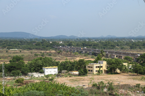 Panoramic view of Chengalpattu city near Chennai, showing the dry Palar River landscape, bridge traffic, lush vegetation, scattered buildings, and distant hills.
