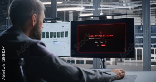 Network Operations Engineer Responds to DDoS Attack Across Data Center Infrastructure, Analyzing System Activity on Dual Monitors to Support Threat Mitigation, Network Security, and Continuity.