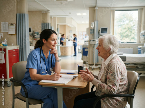Young clinician consults with an elderly woman at a small hospital table
