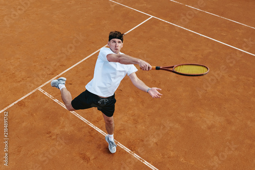 Принти на полотні Caucasian young adult man hitting forehand with racket on clay tennis court