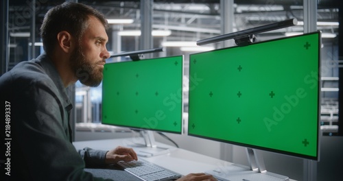 Fotografie IT Professional Working With Dual Green Screen Monitors in Modern Technology Environment, Creating Versatile Chroma Key For Screen Replacement, Digital Interfaces, Corporate Media, and Postproduction