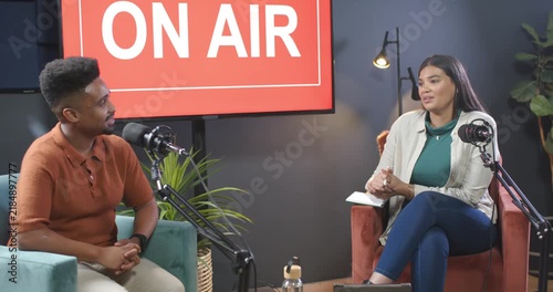 African American co-hosts speaking in studio, ON AIR sign signaling recording with mics, notebook