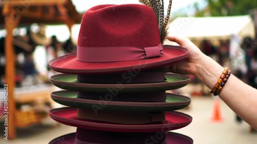 Customer Browsing Stack of Stylish Fedora Hats at Outdoor Market.