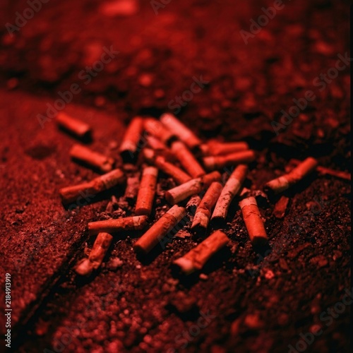 Discarded Cigarette Butts Littered on Textured Ground Under Red Light