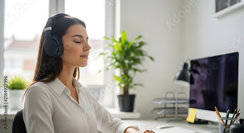 Young woman meditating with headphones at work, finding peace and relaxation in office environment.
