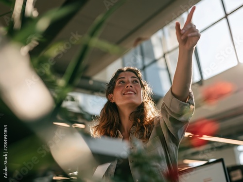 Smiling woman pointing upwards in a bright modern office
