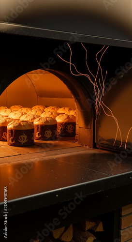 Freshly baked panettone cakes baking inside a glowing warm stone bakery oven