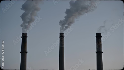 Tall Industrial Smokestacks Emitting Smoke Plumes under Overcast Sky