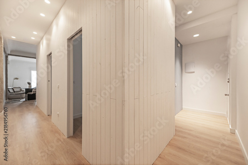 Renovated apartment hallway with white slatted wall paneling dividing paths toward a home office and bedrooms.