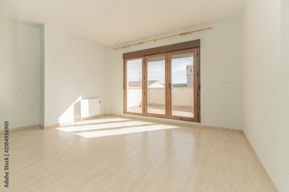 Obraz premium Empty sunlit room with wooden triple French doors opening to a rooftop terrace with church tower view.