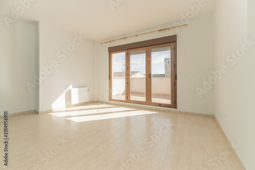 Empty sunlit room with wooden triple French doors opening to a rooftop terrace with church tower view.