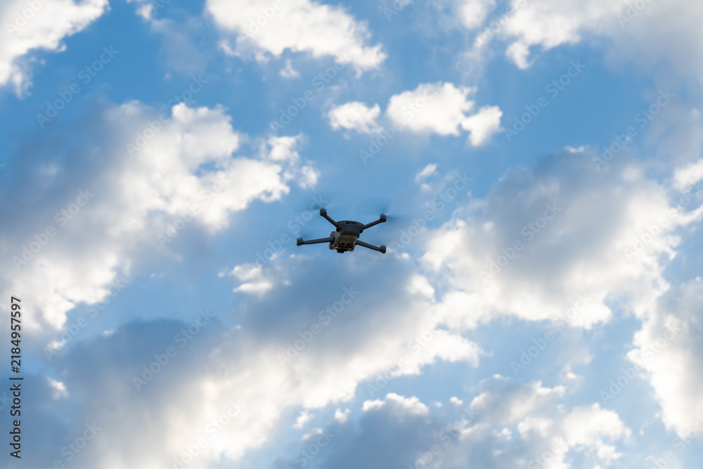 Fototapeta premium Quadcopter drone flying in the blue sky surrounded by white clouds