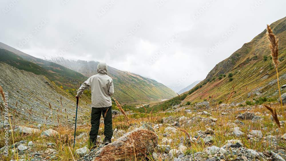 Obraz premium Hiker standing with trekking pole looking at autumn mountain valley near Shkhara glacier in Georgia.