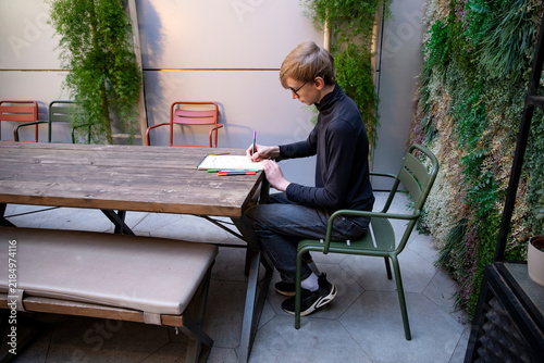 Foto A young boy wearing glasses drawing while sitting at wooden table