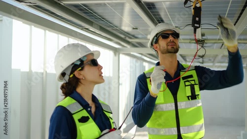 Two professional engineers inspecting solar panels using a digital multimeter on a modern construction site. Teamwork in renewable energy maintenance, wearing safety gear for sustainable power.