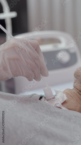 Close-up Hand of nurse suctions mucus from a tube in the throat of a patient who had a tracheostomy and is recovering at home