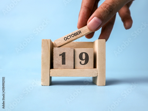 Bild auf Leinwand A woman's hand holds a wooden block with October written on it on a wooden block calendar for October 19th against a light blue background