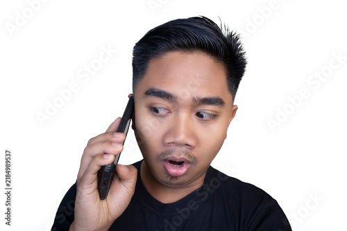 Картината върху платно Surprised Indonesian man wearing a black t-shirt talking on a mobile phone with an open mouth and wide-eyed expression looking sideways against a white background