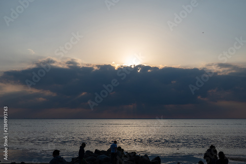 Canvas Print Sunset over the sea under a cloudy sky, with stones in the foreground,  with sil