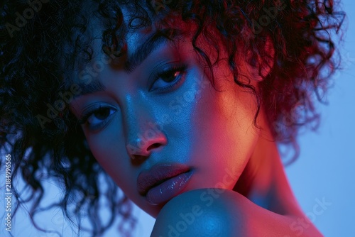 Close-up portrait of an African American woman under neon blue and pink lighting with copy space