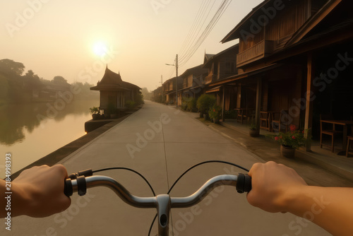 Bicycle hand sunrise river traditional wooden house street peaceful morning Riding bicycle along peaceful riverside street lined with traditional wooden houses at sunrise calm morning atmosphere