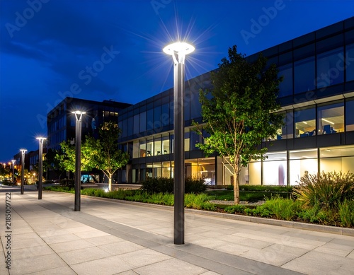 Nighttime view of lit lampposts along a walkway near a modern office building