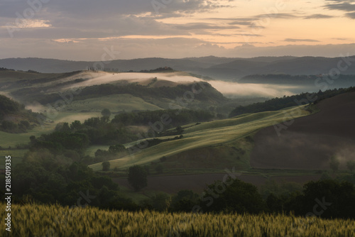 Breathtaking sunrise over the rolling hills of Tuscany, Italy. Scenic landscape featuring morning mist, iconic cypress trees, and a remote rural farmhouse in the beautiful Val d'Orcia valley.