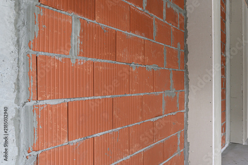 Orange ceramic blocks with vertical ribs, grey mortar joints, uneven edges. adjacent concrete frame, partial doorway, raw construction finish
