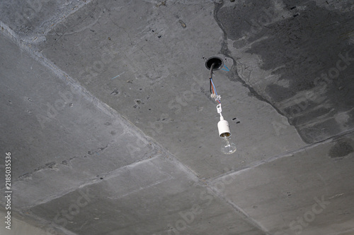 Grey concrete ceiling with visible panel joints, circular ceiling hole, exposed wiring, white E27 socket, clear bulb, raw industrial finish