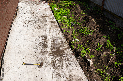 фотографія Light gray concrete apron bordered by brown brick wall and raw soil bed