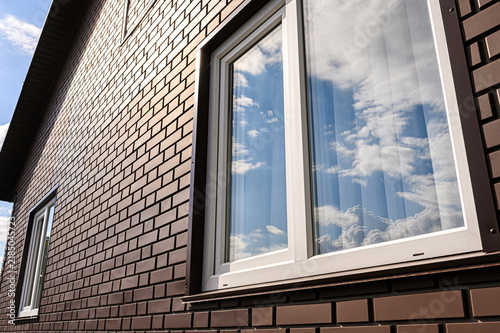 Brown brick facade with white-framed PVC window. cloud reflections in glass panes, dark trim, and textured cladding define modern exterior