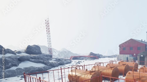 Bright snowy terrain features red buildings and tanks, surrounded by rocky outcrops. The scene captures a cold atmosphere, hinting at an industrial site.