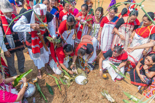 Obraz na płótnie A Mising elder partaking in traditional rice beer as community members arrange ceremonial offerings of fish and rice during the Lhigang rituals in Guwahati,Assam,India on 19 february 2025