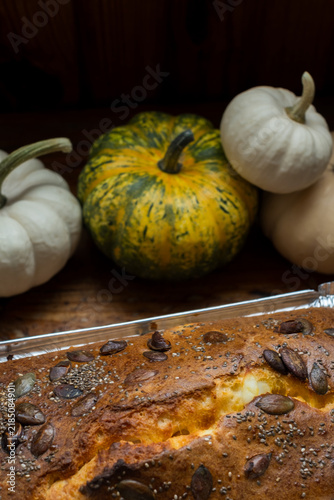 Freshly baked pumpkin loaf cake with seeds on wooden table with pumpkins background for autumn baking concept