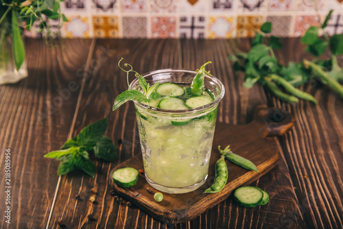 A refreshing cucumber peas mint drink in a glass with ice, surrounded by fresh herbs on a rustic wooden background.