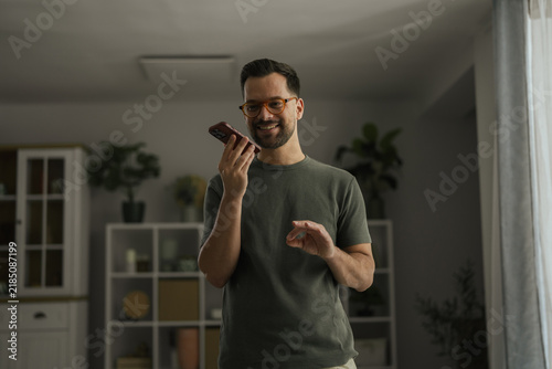 Bild auf Leinwand Young man using voice assistant on smartphone at home