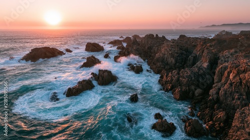 Aerial sunset over turquoise coastline: waves crash on rugged rocks and a glowing horizon