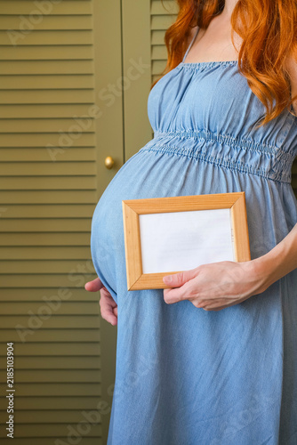 Pregnant woman holding a blank picture frame with copy space for text, illustrating pregnancy, motherhood and family concepts