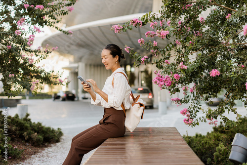 Korean woman relaxing in sunny blooms while using her phone
