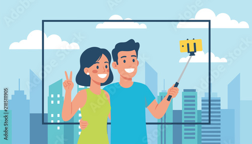 Cheerful young couple taking a selfie together using a phone on a selfie stick in front of city skyscrapers.