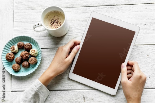 Hands holding tablet beside coffee and chocolates on white table