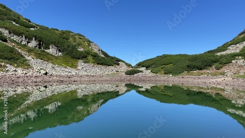 Scenic landscape of the crystal clear glacial Lake Mija with stunning mountain reflections in Parang Mountains, Romania. Nature and travel video, 4K, 60fps.