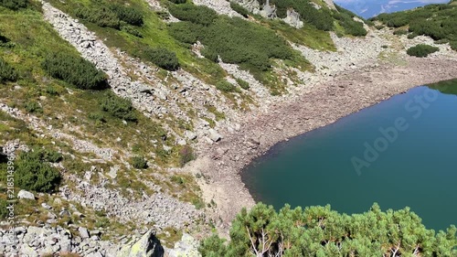 Panning shot of the emerald glacial Lake Mija and rocky alpine slope in Parang Mountains, Romania. Nature and travel video, 4K, 60fps.