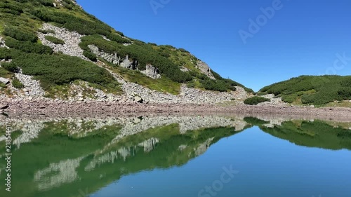 Panning shot of the emerald glacial Lake Mija and rocky alpine slope in Parang Mountains, Romania. Nature and travel video, 4K, 60fps.