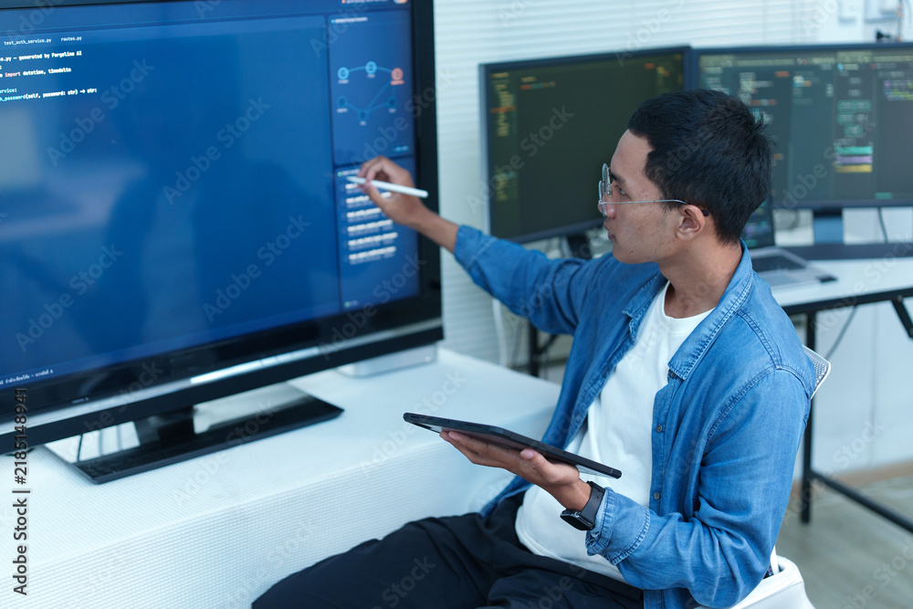 Fototapeta premium Programmer Analyzing Code and Digital Data on Multiple Screens