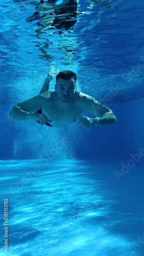 Underwater view of a man performing a headfirst dive into a clear blue swimming pool, creating bubbles and dynamic movement beneath the surface.